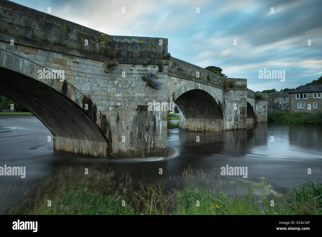 Vue panoramique du pont enjambant la rivière Wharfe s'écoule doucement à travers Burnsall village, sur soirée d'été avec ciel bleu - Vallées du Yorkshire, England, UK. Banque D'Images