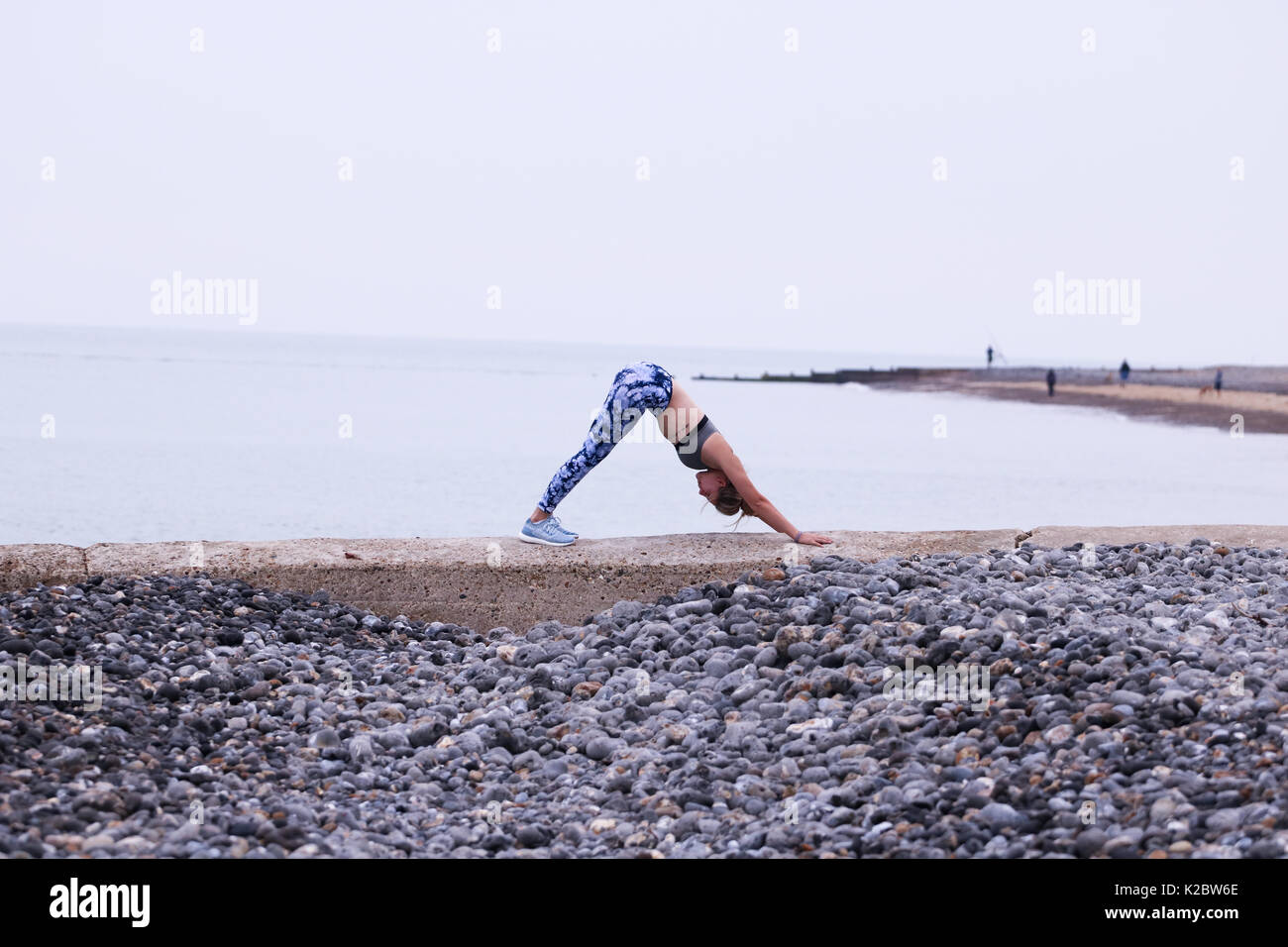 Young woman doing yoga on sea wall en Cromer, Norfolk, Royaume-Uni. Banque D'Images