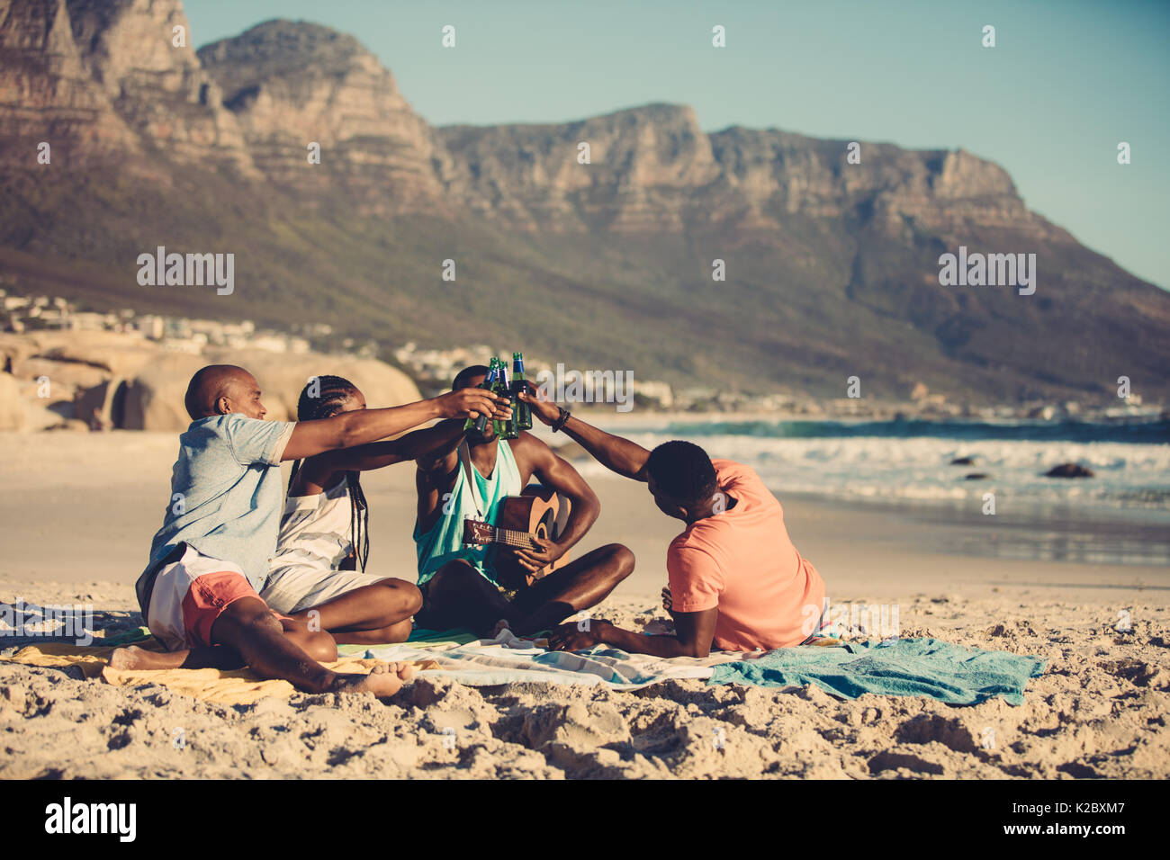 Les jeunes hommes avec un woman toasting bières sur la plage. Groupe d'amis à faire la fête sur les vacances à la plage. Banque D'Images