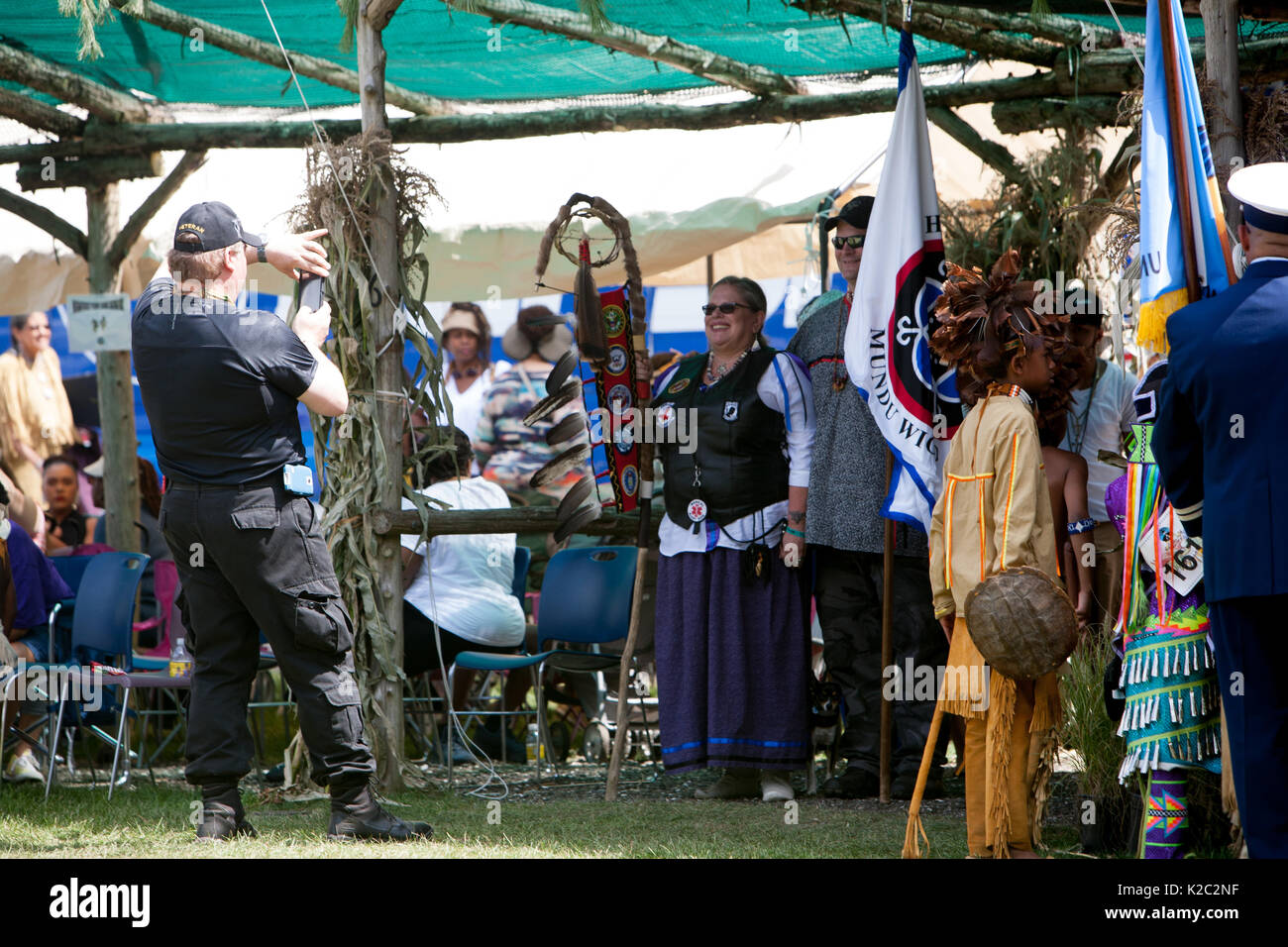 Un homme utilise un téléphone cellulaire pour prendre des photos de deux Autochtones qui tiennent leur personnel et de l'Aigle Drapeau Tribal. Banque D'Images