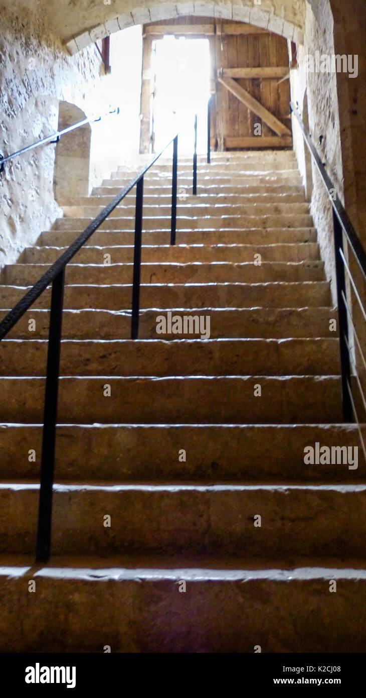 Une vue vers le haut des escaliers en pierre sombre escalier vers une porte en bois avec une lumière qui brillait à travers l'arbre en haut Banque D'Images