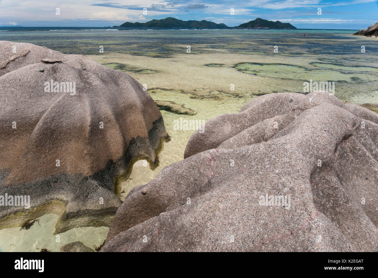 Les rochers de granit et de paysages d'eau peu profonde, l'Anse Saint-Jean, l'île de La Digue, Praslin Island dans l'arrière-plan, République des Seychelles Banque D'Images