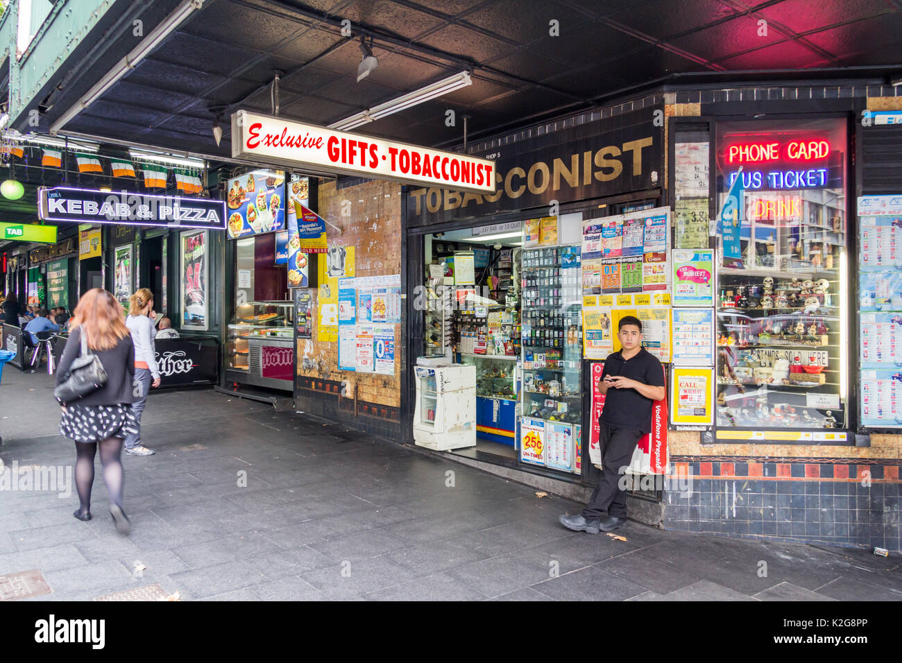Un jeune homme contre un magasin de tabac salons sur un coin de rue George, Sydney, Australie Banque D'Images
