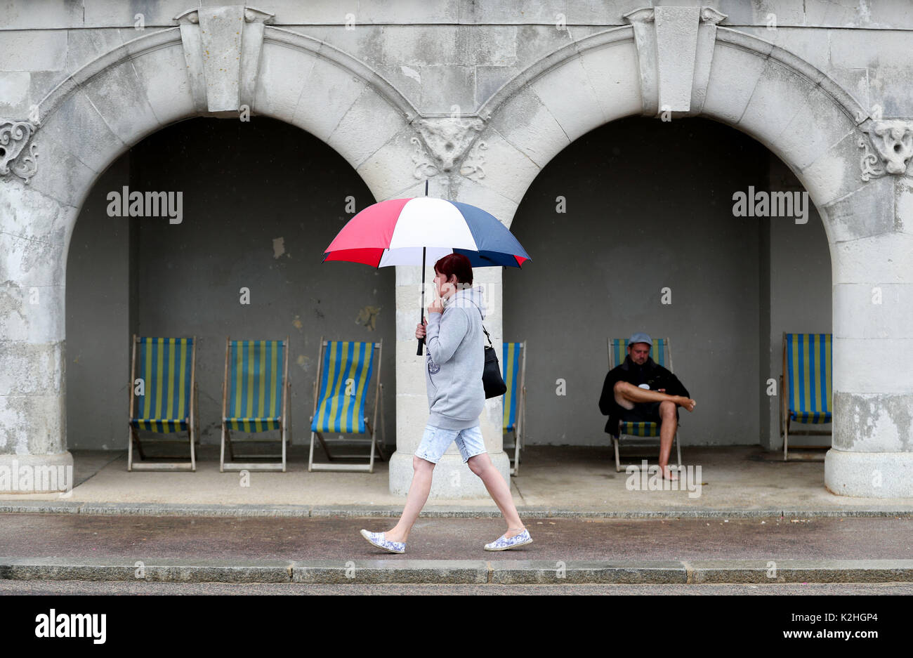 Une dame se promène avec un parapluie le long de l'esplanade sur la plage de Bournemouth dans le Dorset. Banque D'Images