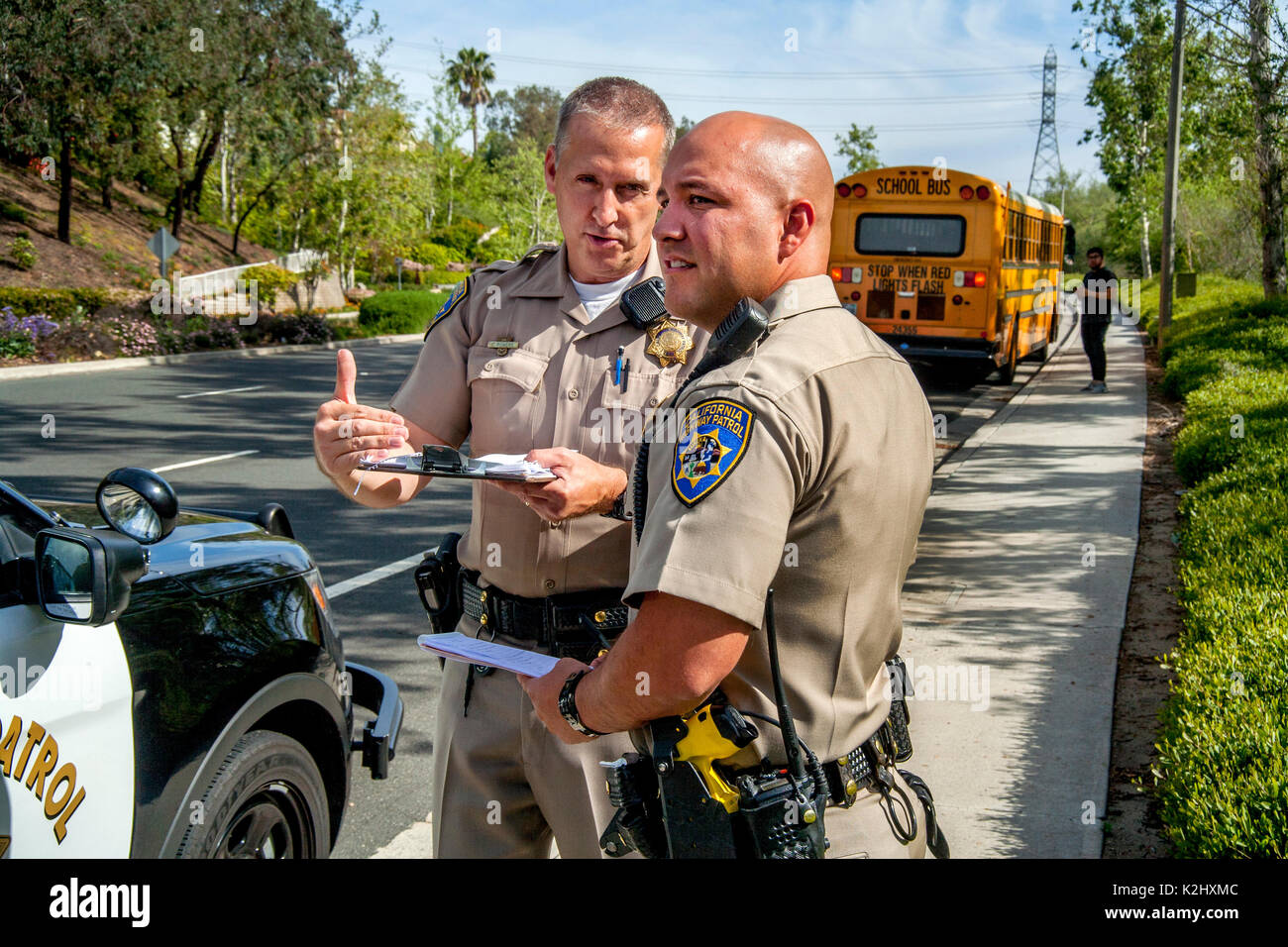 Des policiers en uniforme et caucasienne hispaniques observer l'état des routes menant à un accident d'autobus dans la région de Laguna Hills, CA. Remarque Les bus et chauffeur en arrière-plan. Banque D'Images