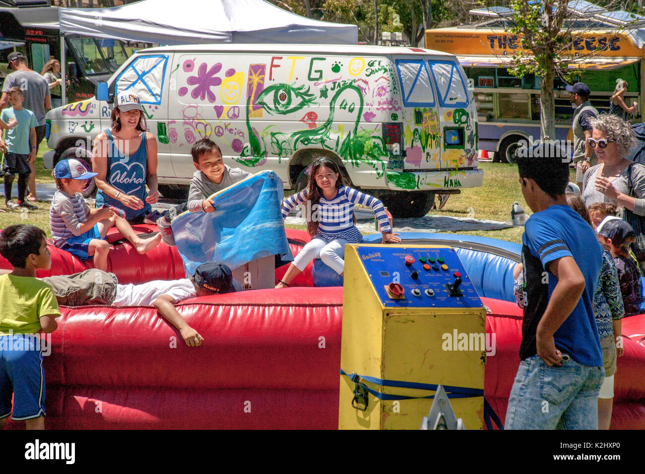 Les enfants de profiter d'une balade qui imite un surf au Costa Mesa, CA, festival communautaire. Remarque Le panneau de configuration et van en arrière-plan décoré par des artistes amateurs locaux. Banque D'Images