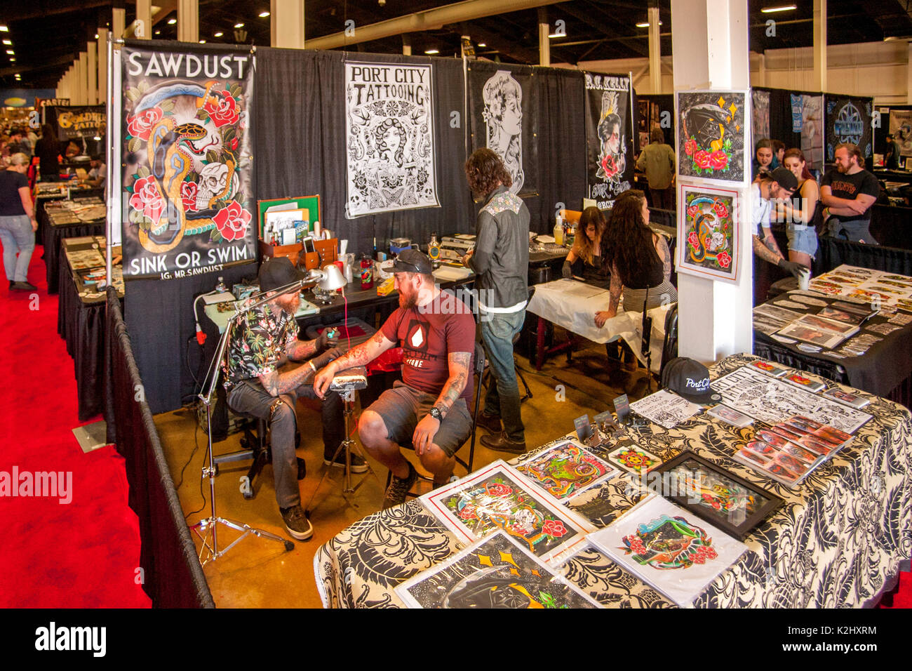 Entouré par des échantillons de l'art du tatouage, un client est assis pour un artiste de tatouage lors d'une convention de tatouage à Costa Mesa, CA. Banque D'Images