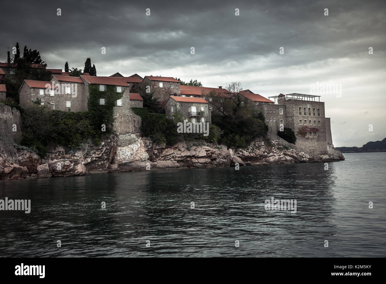 Vieux bâtiments antiques sur l'île de Sveti Stefan entouré par l'eau de mer sur les côtes pendant le coucher du soleil avec ciel dramatique en Europe pays Monténégro Banque D'Images