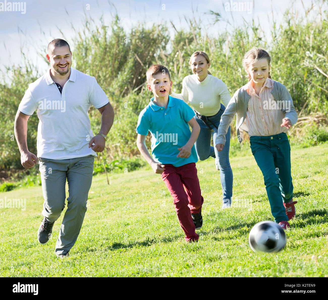 La famille de quatre personnes de race blanche jouant joyeusement dans le football together outdoors Banque D'Images