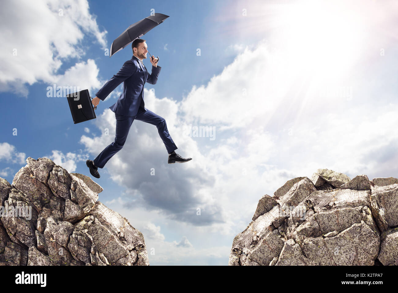 Businessman with umbrella jumping sur les montagnes. Banque D'Images