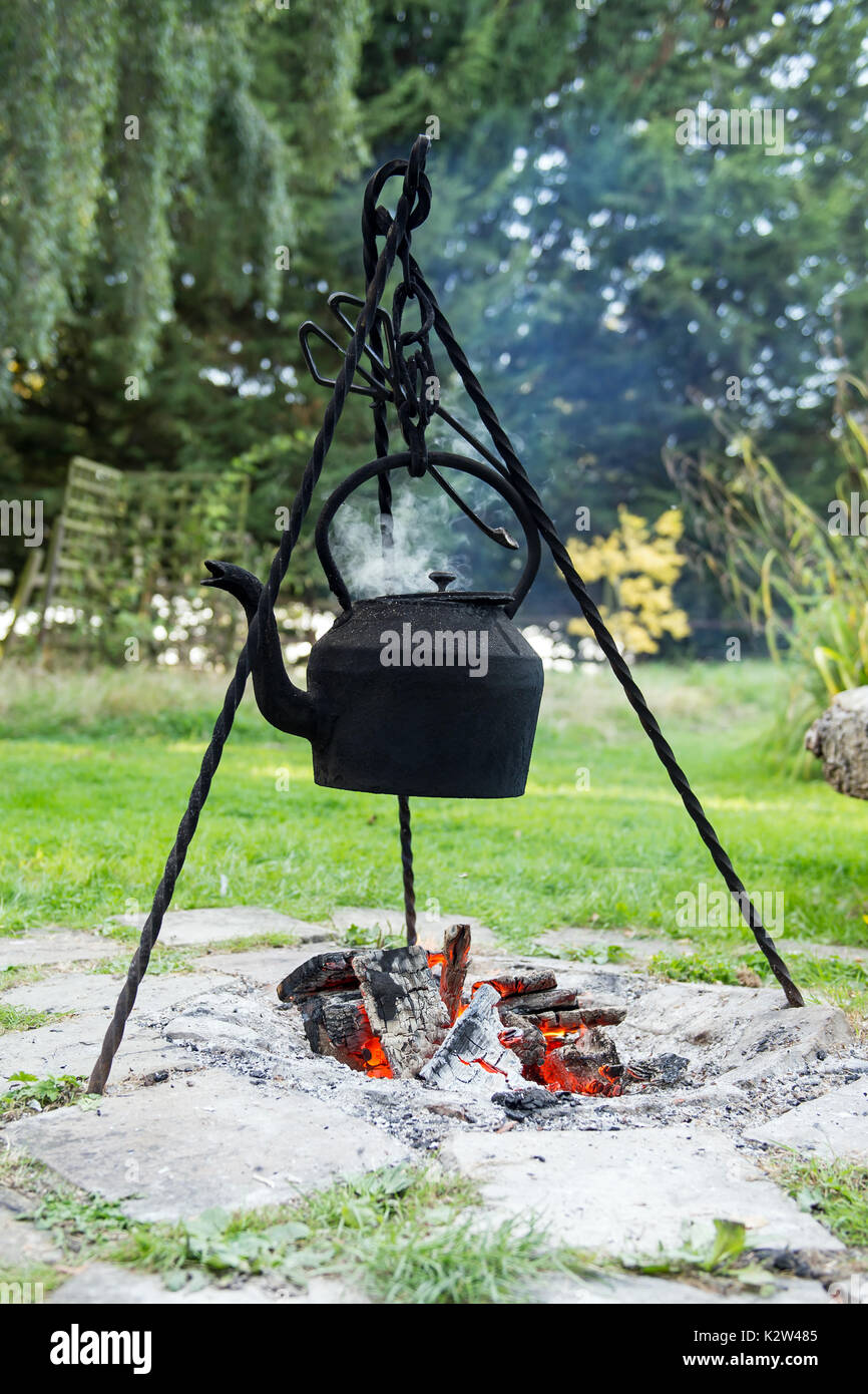Une bouilloire noircie se bloque sur un trépied sur un feu ouvert Banque D'Images