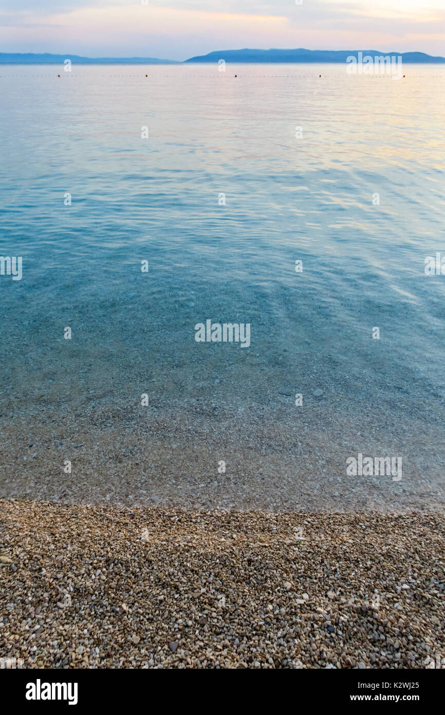 La mer propre calme avec plage de galets et de terre à l'horizon. Banque D'Images