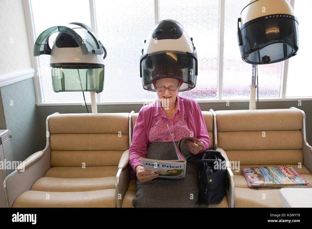 Personne âgée retraitée ayant ses cheveux séché dans un sèche-linge hotte portant des bigoudis dans un salon de coiffure dames, Angleterre, Royaume-Uni Banque D'Images