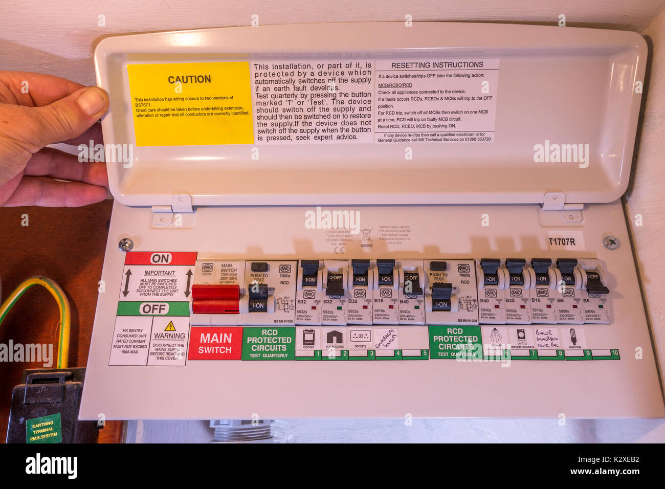 Le pouce et l'homme maintenant ouvrir le couvercle d'une unité de consommation d'électricité nouvellement montée, avec de multiples commutateurs on/off. Angleterre, Royaume-Uni. Banque D'Images