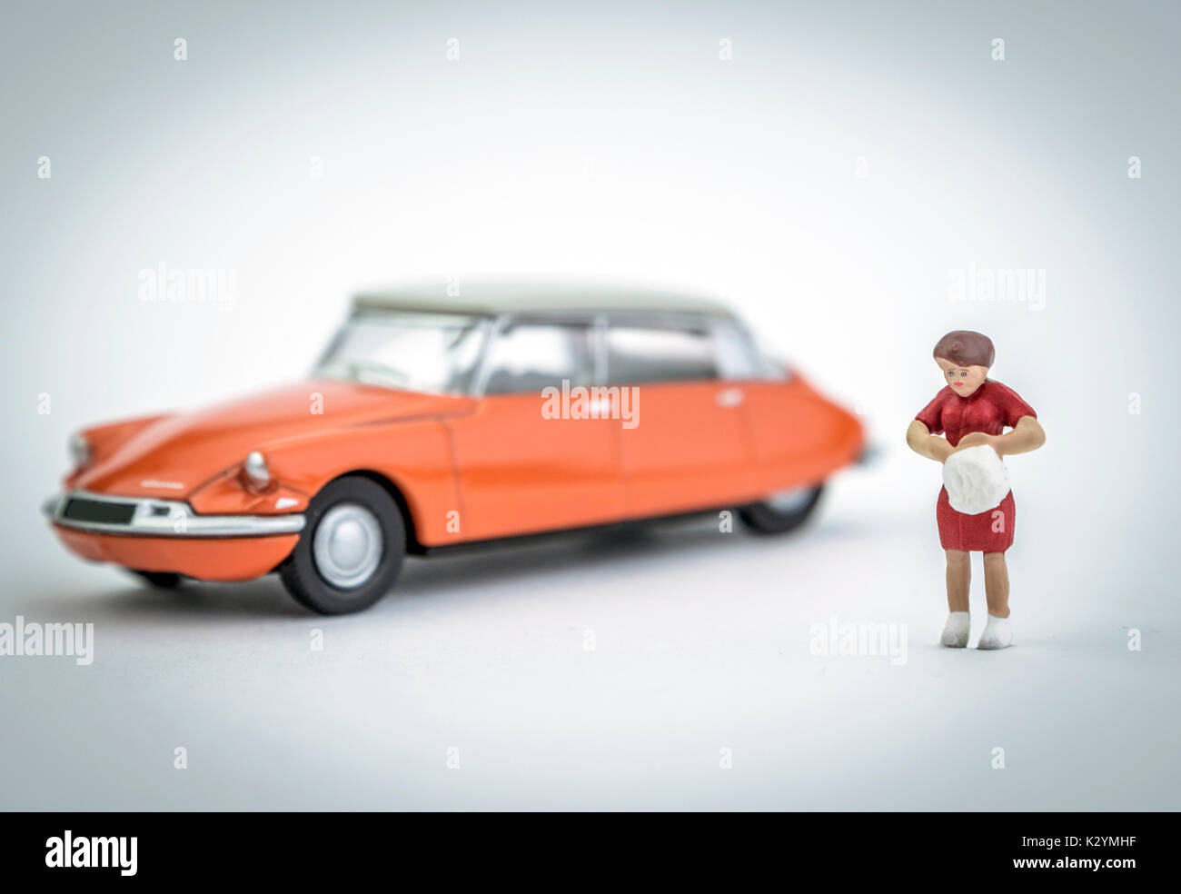 La figure d'une femme miniature vient de garé sa voiture orange vintage Banque D'Images