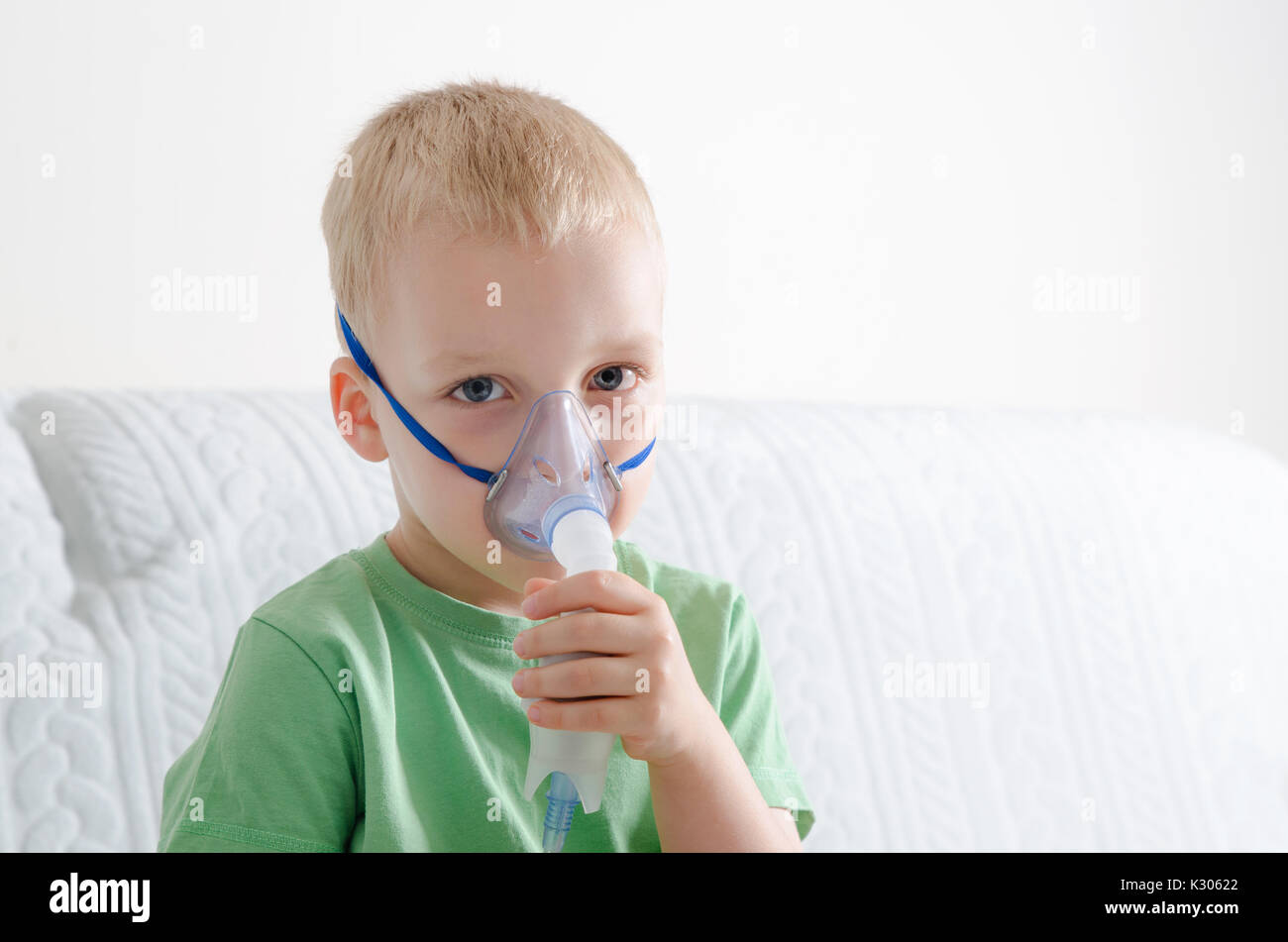 petit garçon malade avec inhalateur pour le traitement de la toux. enfant  malade faisant de l'inhalation sur son lit. saison de la grippe.  intervention médicale à domicile. intérieur et vêtements aux couleurs