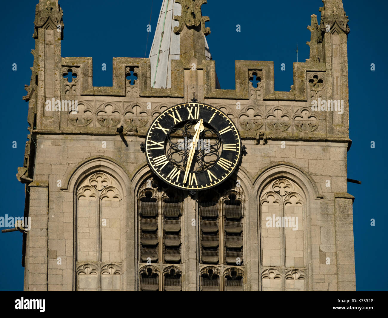 Horloge ensoleillée avec chiffres romains dorés et visage noir sur la tour de l'église en pierre Banque D'Images