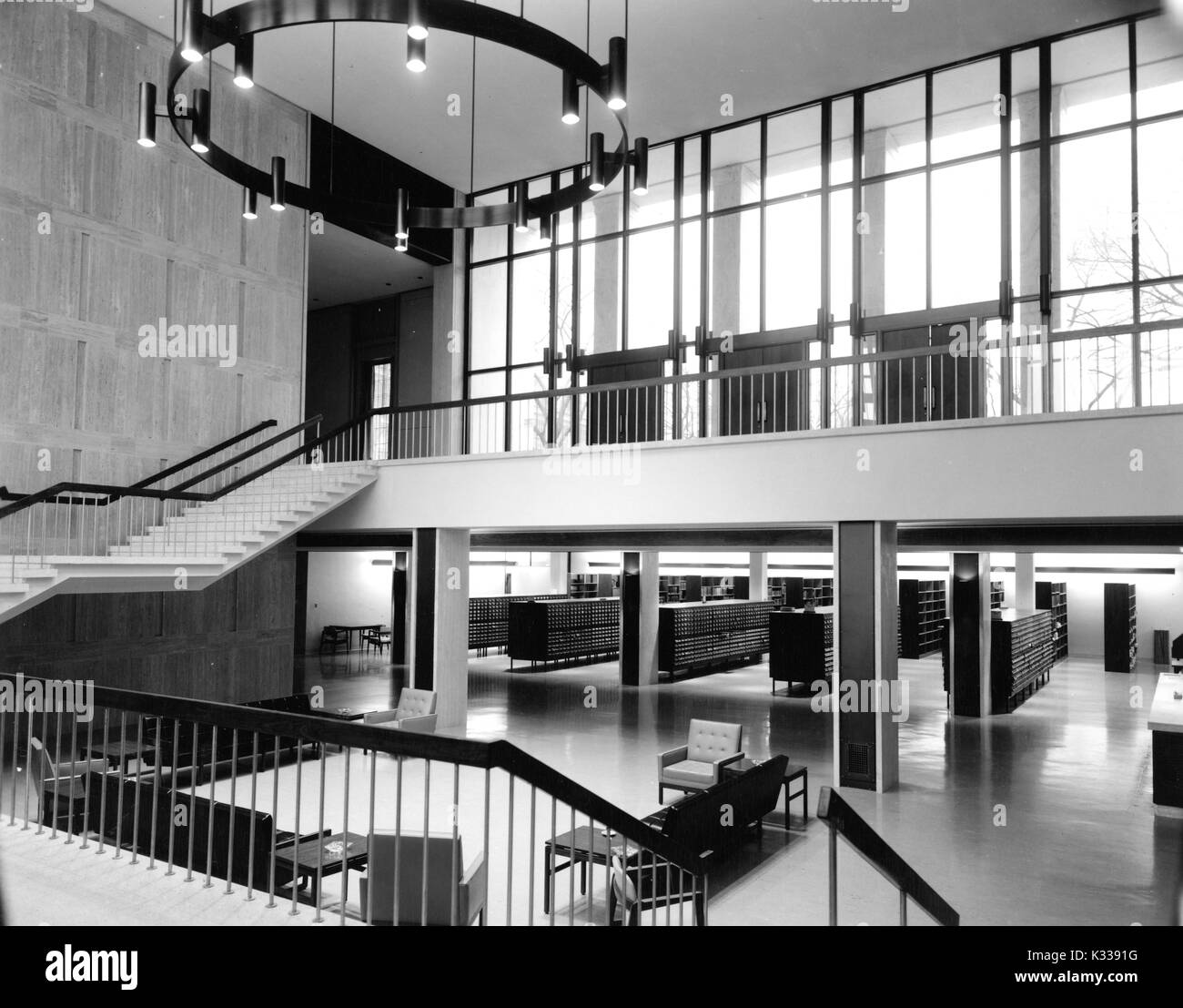 L'intérieur de Milton S Eisenhower Library à sa conception originale, y compris le foyer ouvert et un escalier entre Q et M, avec des sièges à l'avant, des piles de catalogues dans l'arrière-plan, et le bureau de service à la droite, sous les portes et fenêtres en verre de grande taille au plus haut niveau, et un grand lustre, Baltimore, Maryland, 1965. Banque D'Images