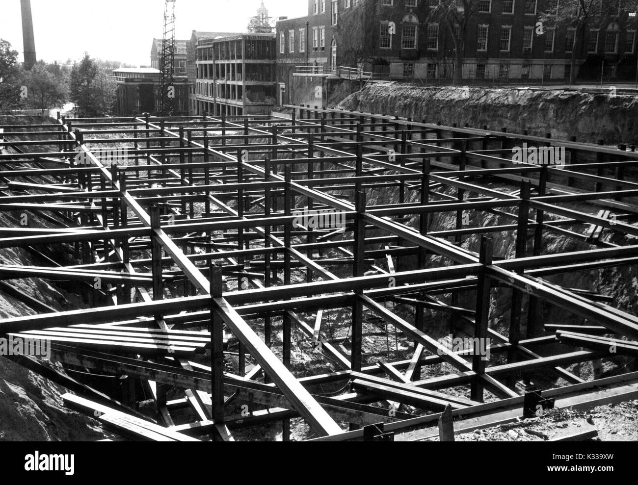 Au cours des premières étapes de la construction de la Milton S Eisenhower Library à l'Université Johns Hopkins, poutres d'acier sont empilés et disposés en place depuis la fondation de l'édifice, avec des poutres et des planches jonché autour du site de saleté, avec des bâtiments du campus visible à l'arrière-plan, y compris Krieger Hall (initialement appelé Rowland Hall), un laboratoire de mathématiques et des capacités, Baltimore, Maryland, 1963. Banque D'Images