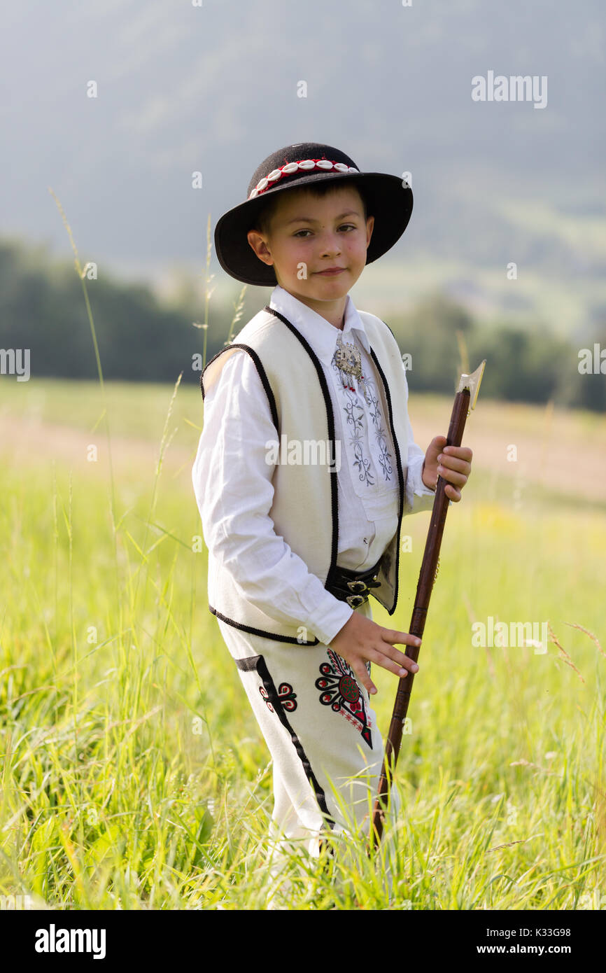 Enfant Garçon en robe traditionnelle goral, hat et ax se dresse sur meadow en montagnes polonaises. Portrait vertical avec une faible profondeur de champ Banque D'Images