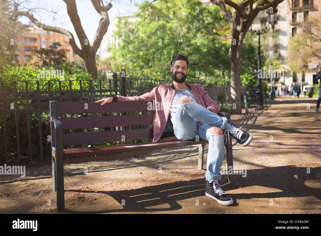 Une photo de jeune homme assis sur le banc dans le parc. Il est souriant. Banque D'Images