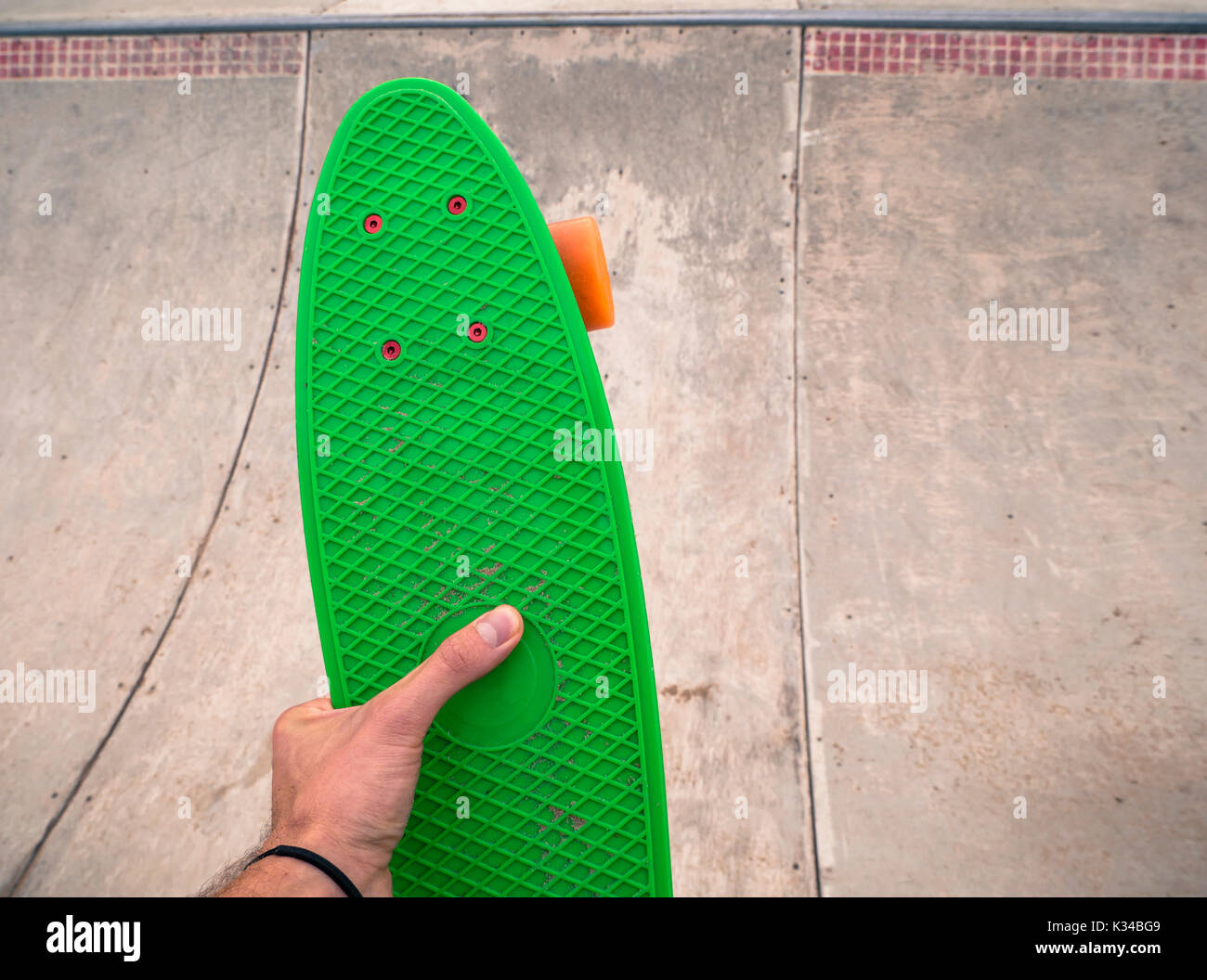 Male hand holding a green conseil penny dans un skatepark. Banque D'Images