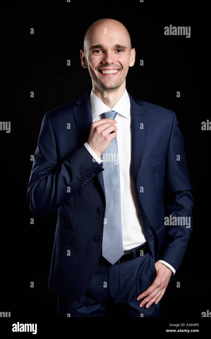 Young smiling businessman holding sa cravate. Portrait sur fond noir. Banque D'Images