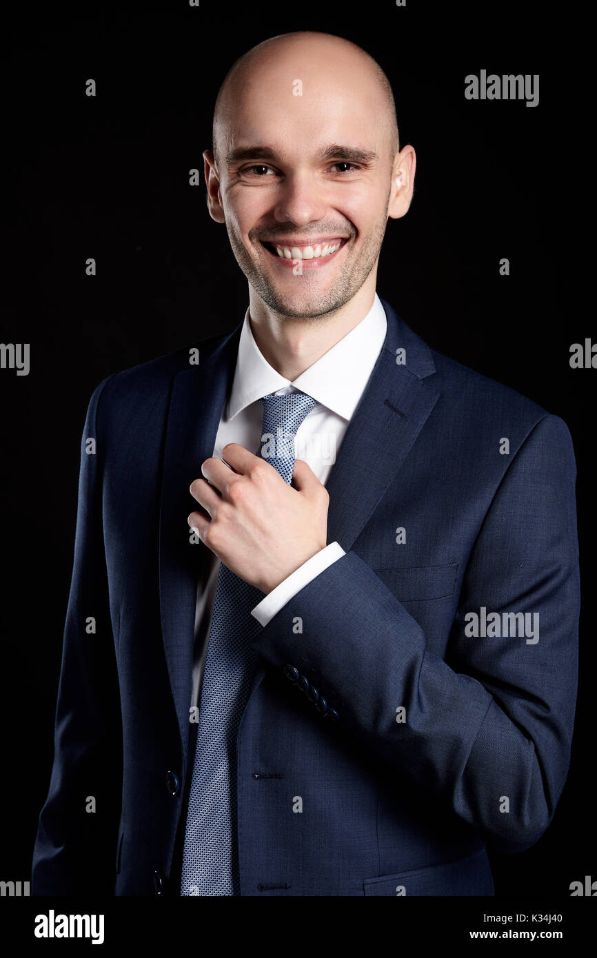 Portrait of smiling man holding sa cravate. Portrait sur fond noir. Banque D'Images