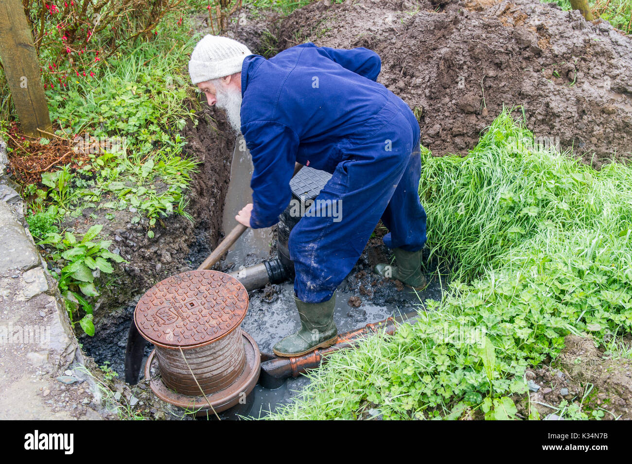 Plombier creuse un trou pour réparer les drains bloqués en Irlande. Banque D'Images