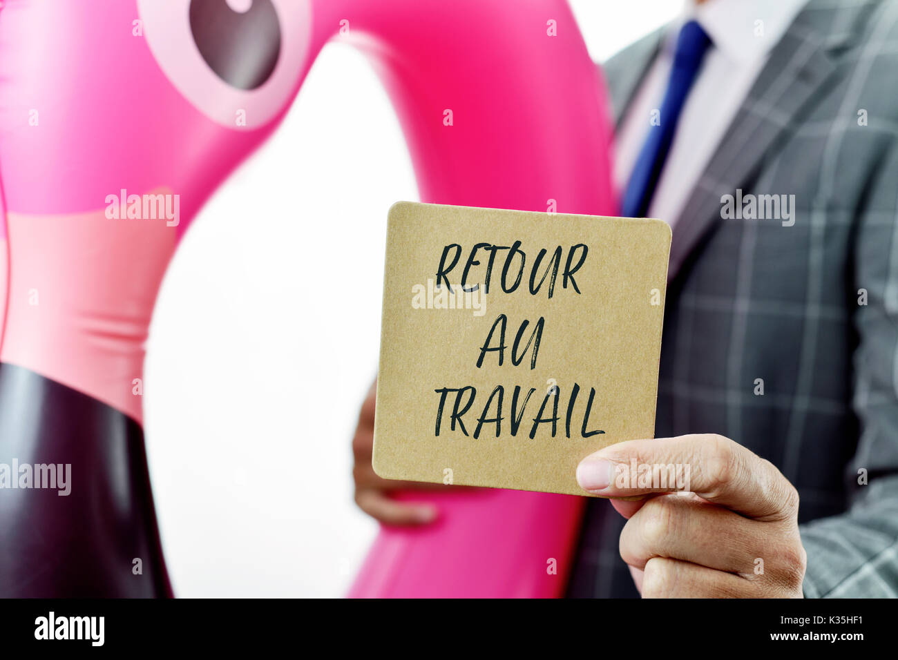 Libre d'un young caucasian businessman portant un anneau de bain en forme de flamant rose montrant une pancarte marron avec le texte retour au travail Banque D'Images