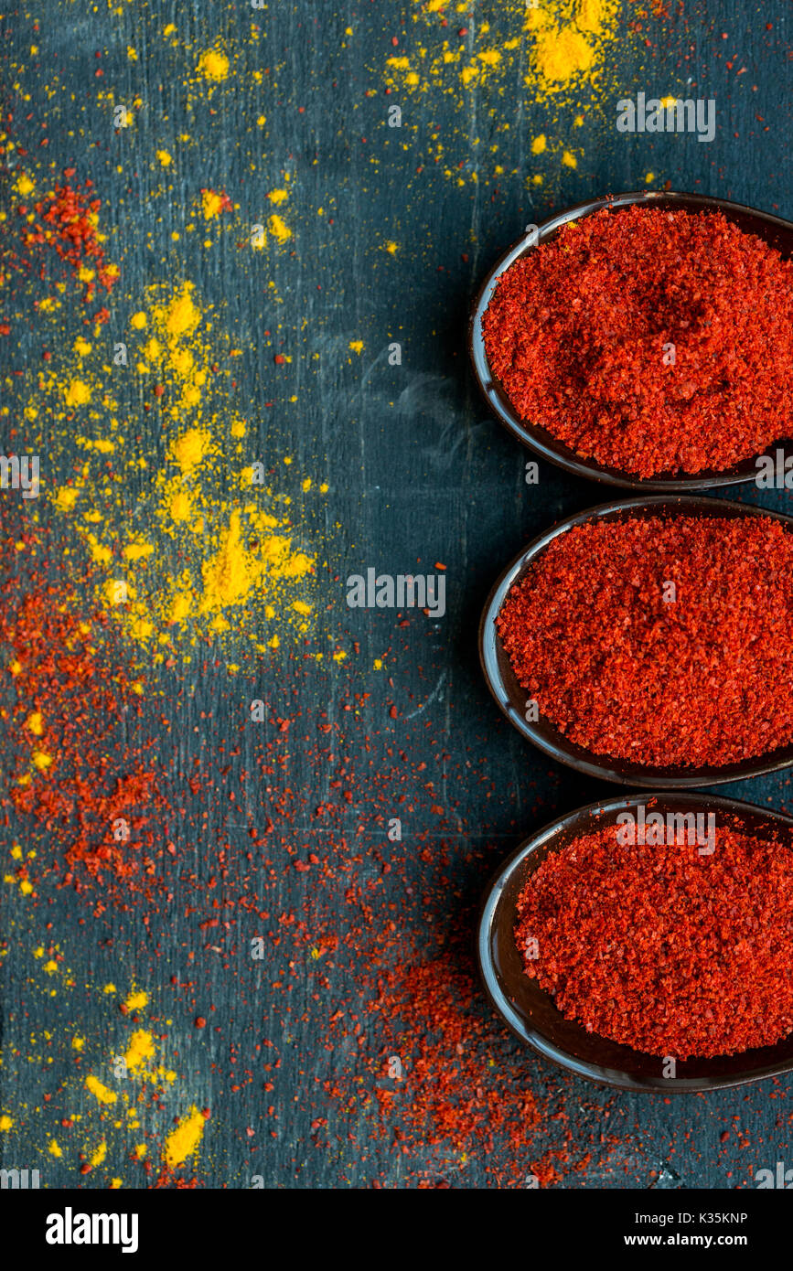 Vue de dessus de cuillères remplies d'épices paprika rouge foncé sur fond de bois recouvert de poudre de curcuma et de paprika Banque D'Images Vue de dessus de cuillères remplies d'épices paprika rouge foncé sur fond de bois recouvert de poudre de curcuma et de paprika Banque D'Images
