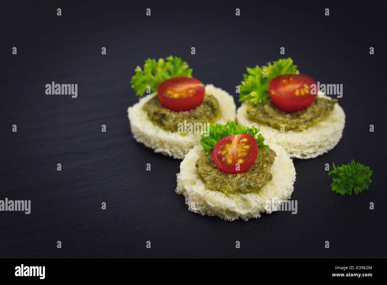 Finger Food pour partie des Canape sauce pesto sur le dessus de la tomate et le persil feuille sur la plaque en ardoise noire Banque D'Images