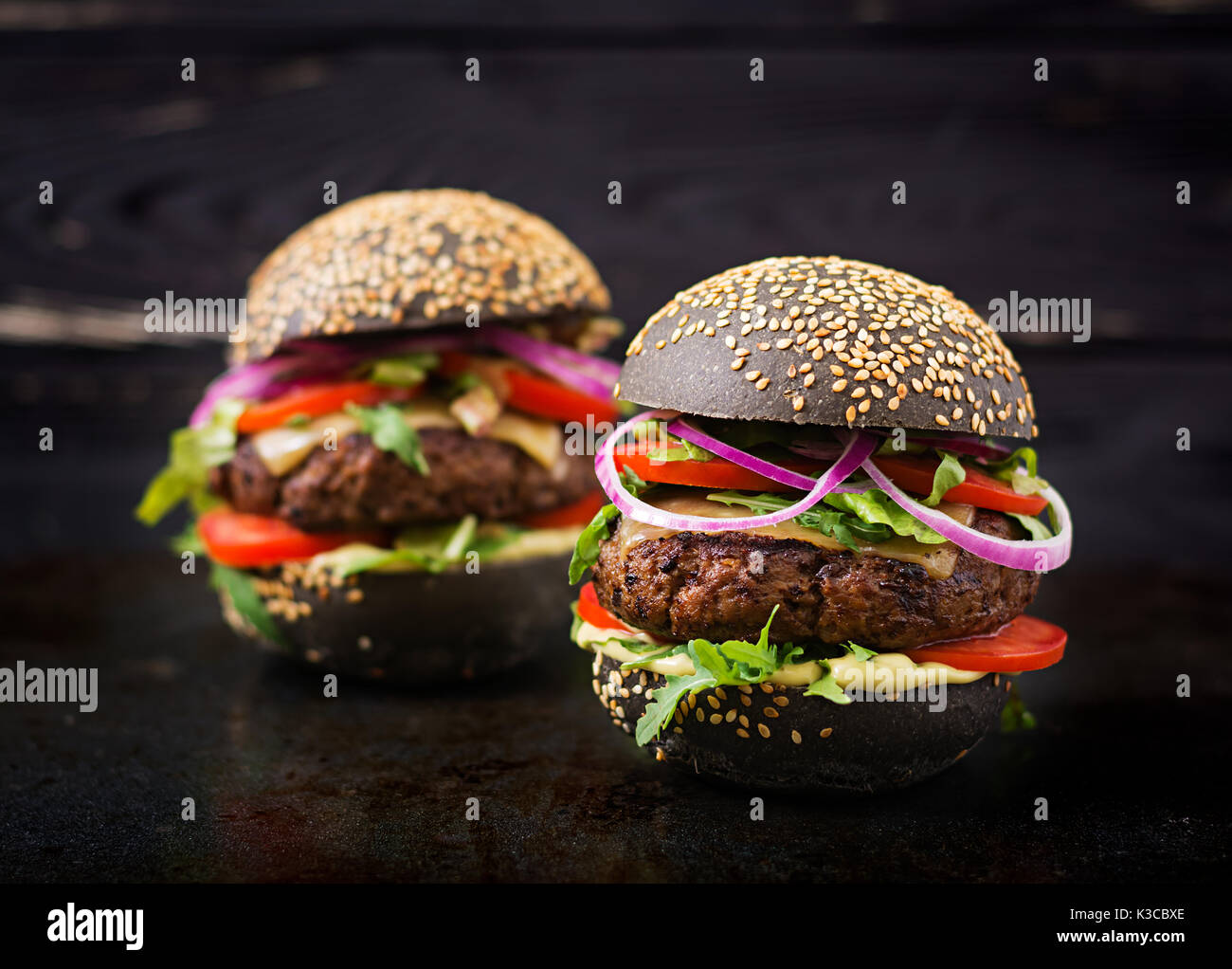 Big sandwich noir - noir avec hamburger burger de boeuf juteux, fromage, tomate et oignon rouge sur fond noir Banque D'Images
