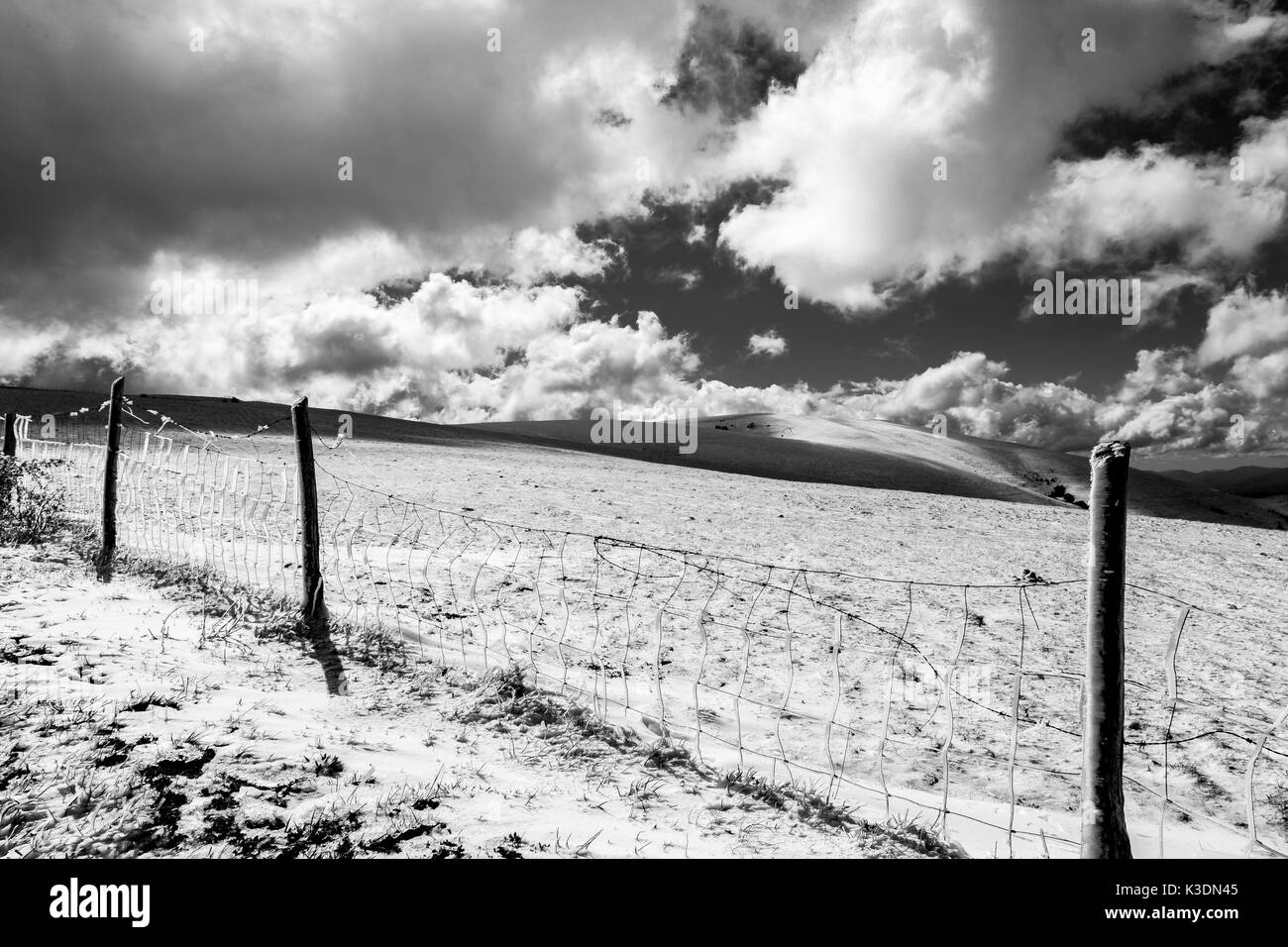 Les champs de la montagne couverte de neige, avec une clôture en premier plan, sous un ciel profond avec des nuages blancs Banque D'Images