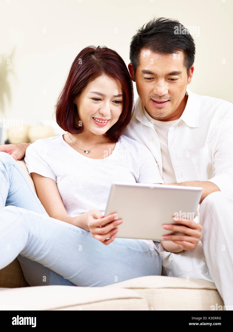 Asian couple sitting on sofa using digital tablet ensemble à la maison. Banque D'Images