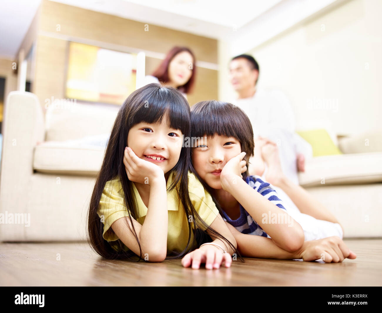 Frère et soeur d'asie se trouvant à l'avant sur le plancher avec les parents dans l'arrière-plan. Banque D'Images