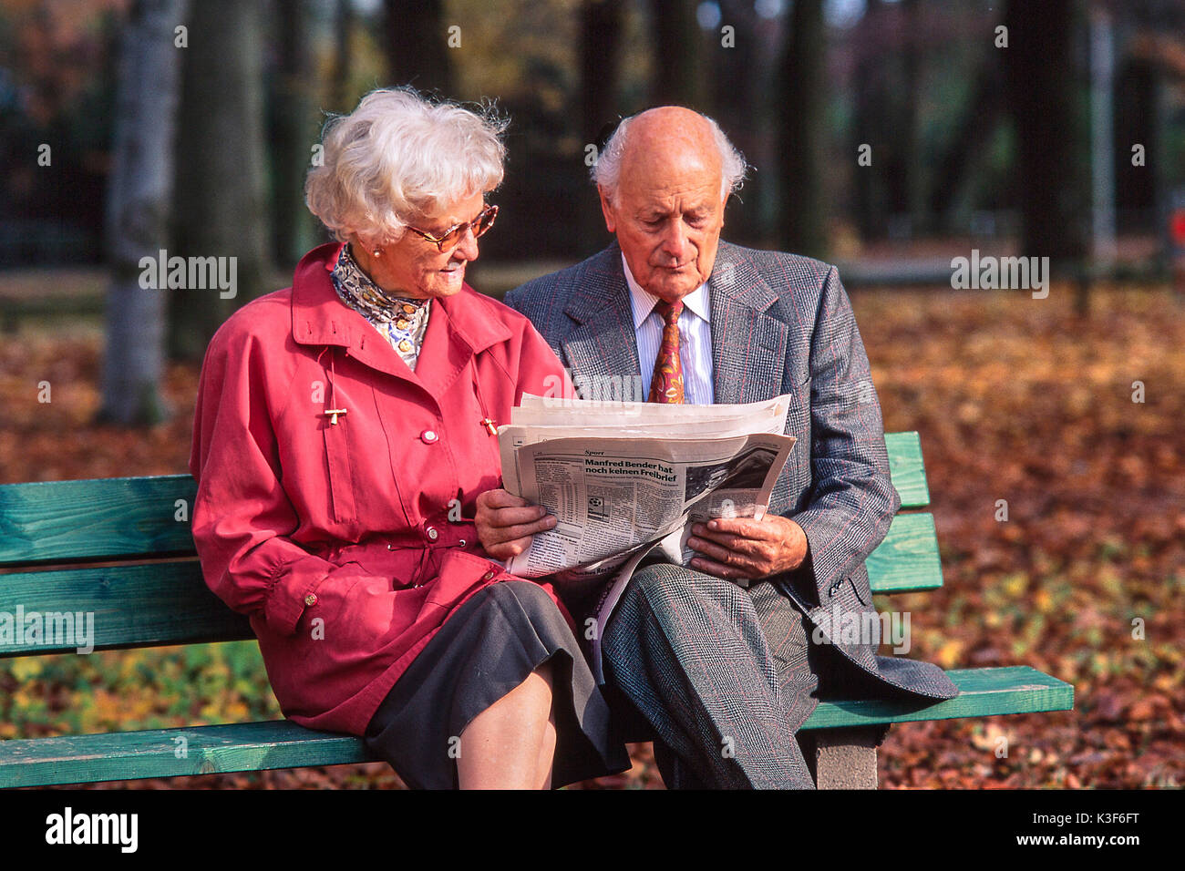 Couple de personnes âgées se lit sur un banc au parc-journal en bois Banque D'Images