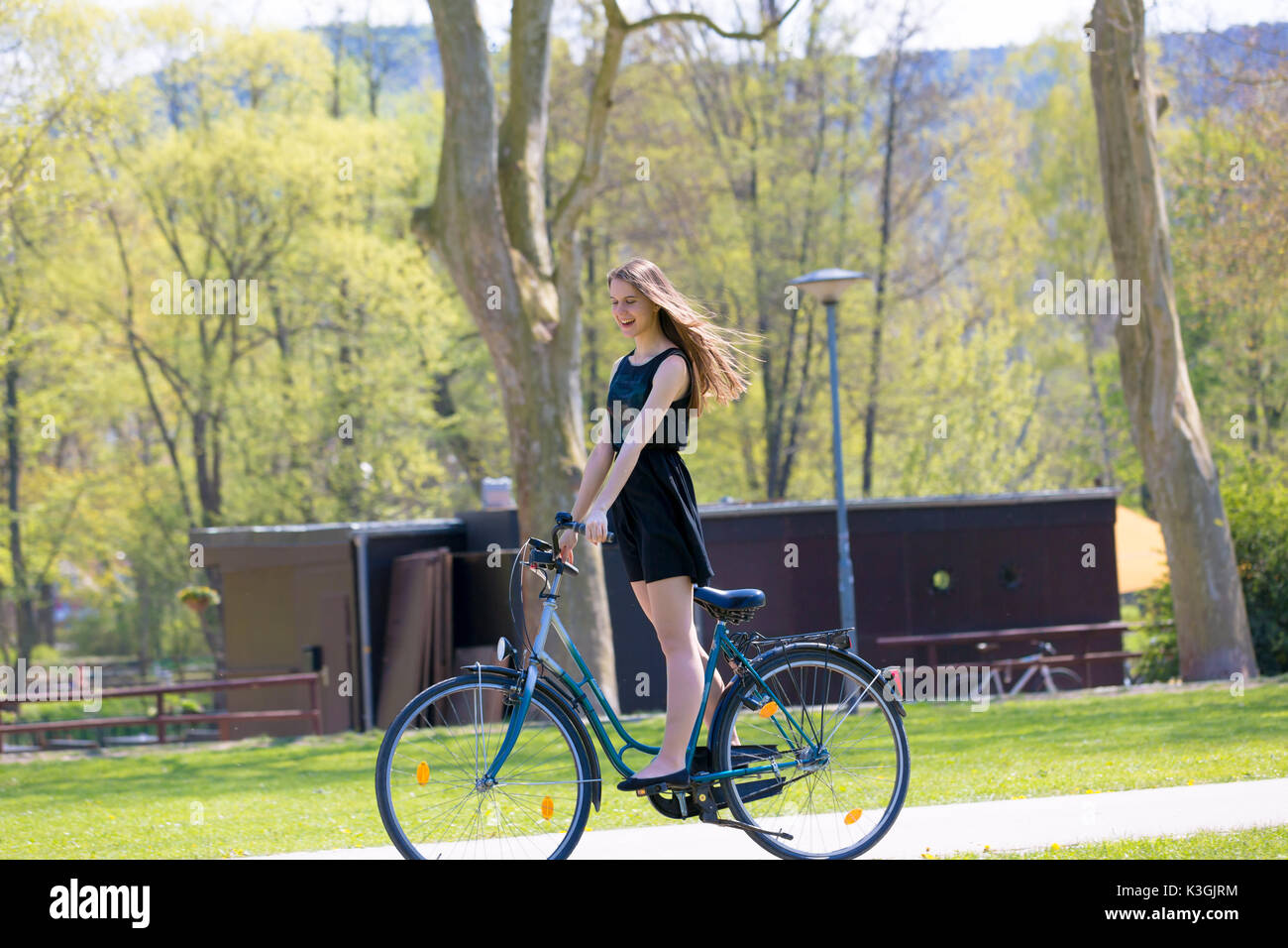 Vue Portrait of Girl sur location portant sur noir robe courte. Jeune femme heureuse équitation le long de la route sur vert printemps parc extérieur. Jeune fille sportive ri Banque D'Images