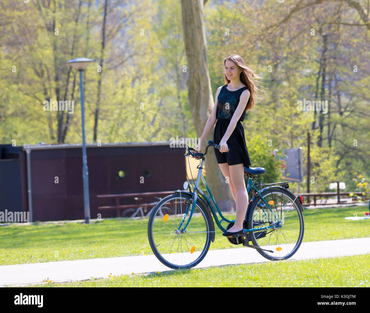 Vue Portrait of Girl sur location portant sur noir robe courte. Jeune femme heureuse équitation le long de la route sur vert printemps parc extérieur. Jeune fille sportive ri Banque D'Images