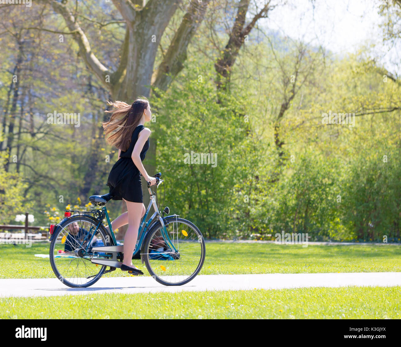 Vue Portrait of Girl sur location portant sur noir robe courte. Jeune femme heureuse équitation le long de la route sur vert printemps parc extérieur. Jeune fille sportive ri Banque D'Images