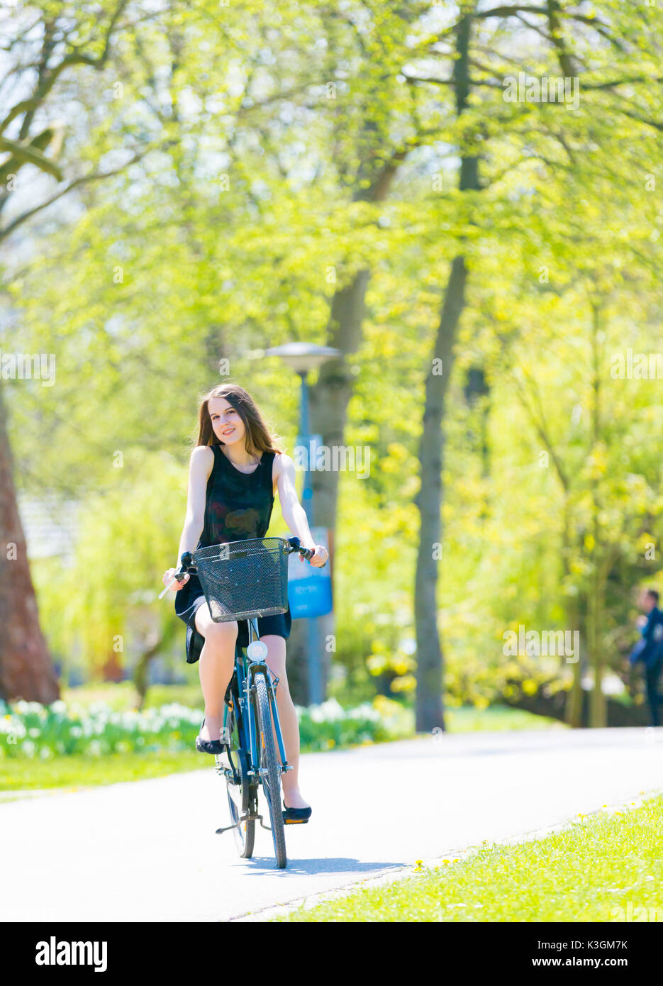 Vue Portrait of Girl sur location portant sur noir robe courte. Jeune femme heureuse équitation le long de la route sur vert printemps parc extérieur. Jeune fille sportive ri Banque D'Images