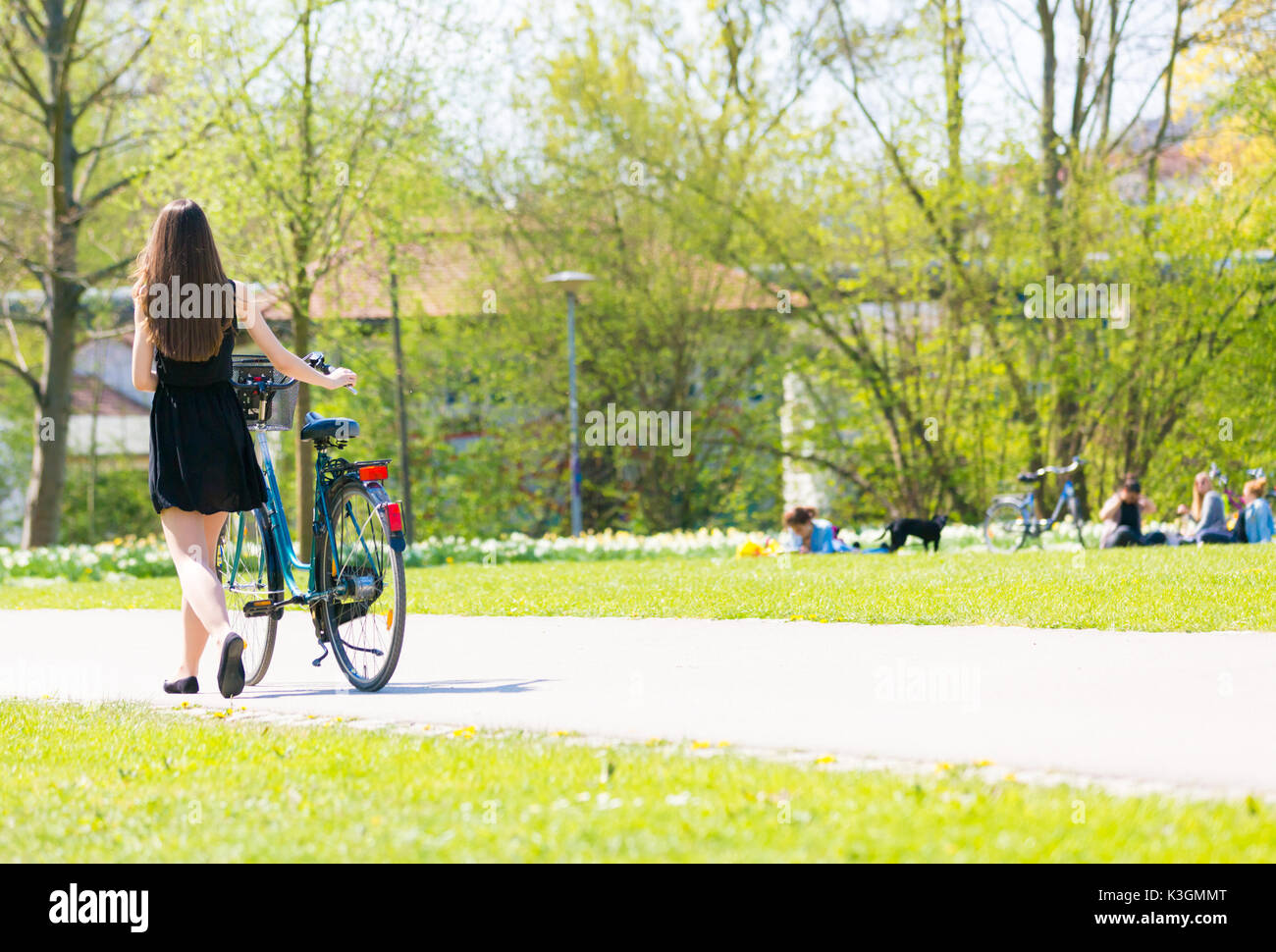 Vue arrière de la fille sur location portant sur noir robe courte. Jeune femme équitation le long de la route sur vert printemps parc extérieur. Jeune fille sportive équitation un bic Banque D'Images