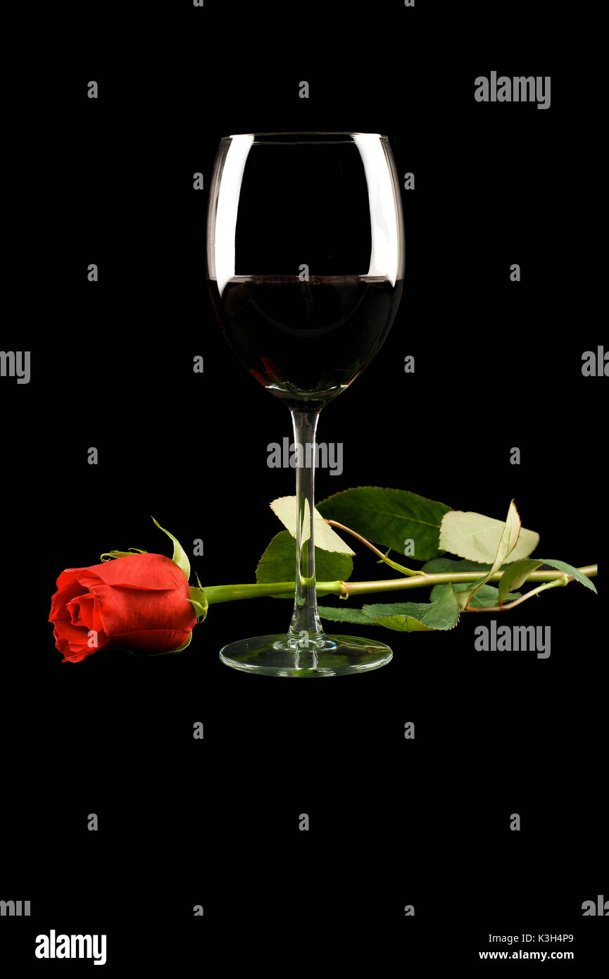 Un verre de vin rouge et une rose rouge à une tige lors d'un repas romantique. Banque D'Images