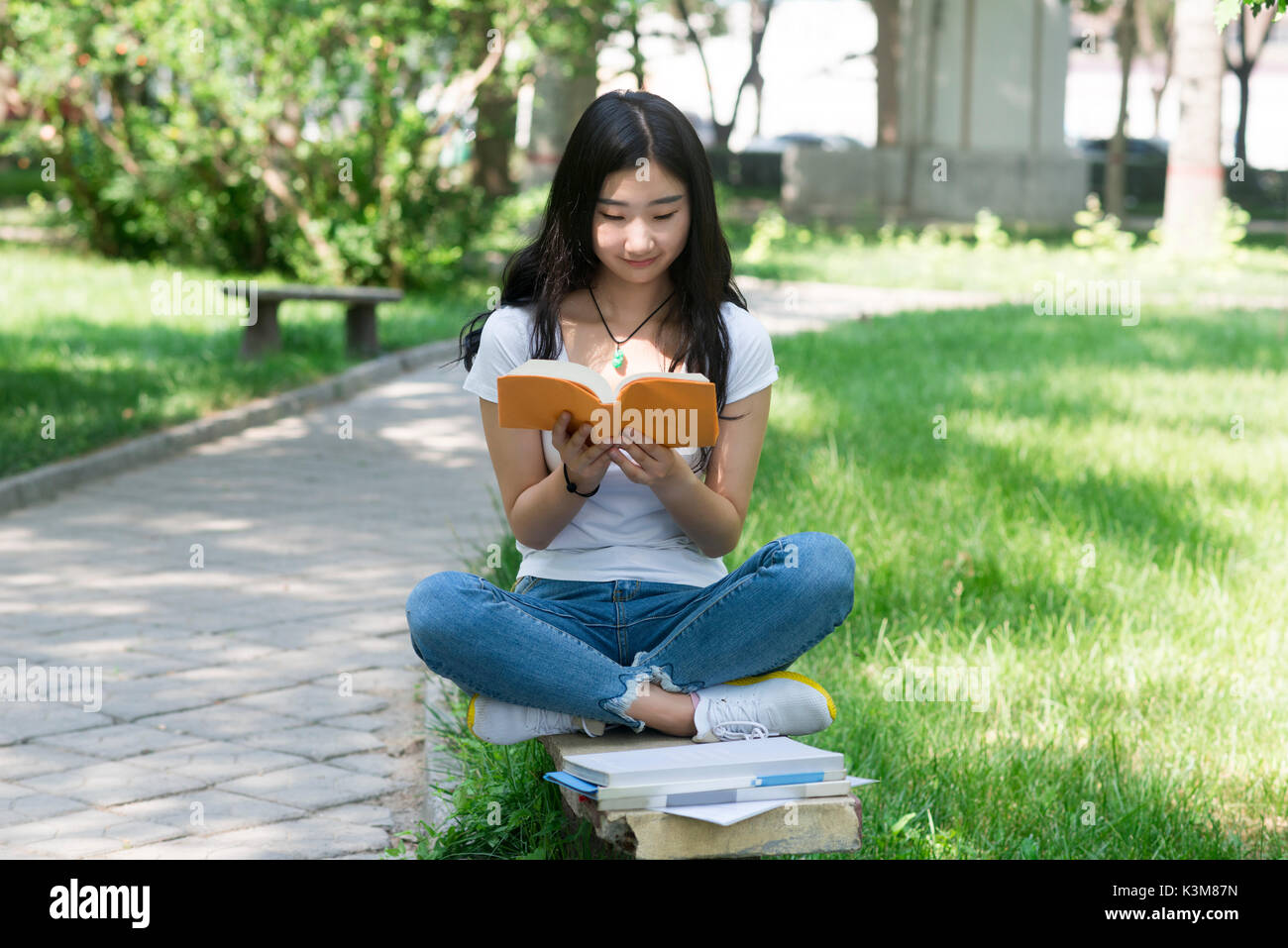 L'élève fille tient un livre à lire. sur le banc. Banque D'Images