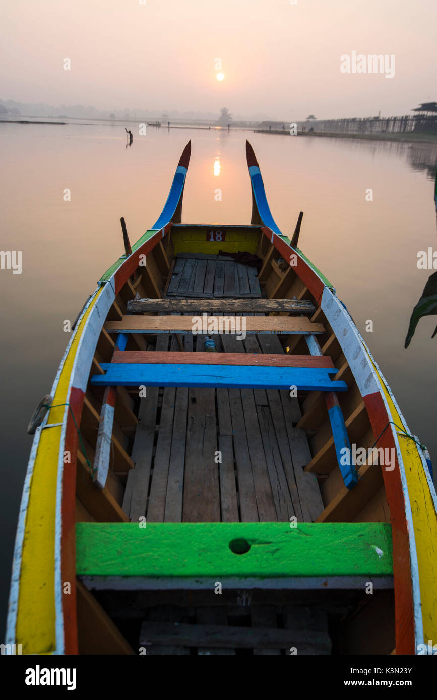 Amarapura, région de Mandalay, Myanmar. Bateaux colorés amarrés sur les rives de la lac Taungthaman au lever du soleil, avec l'U Bein bridge en arrière-plan. Banque D'Images