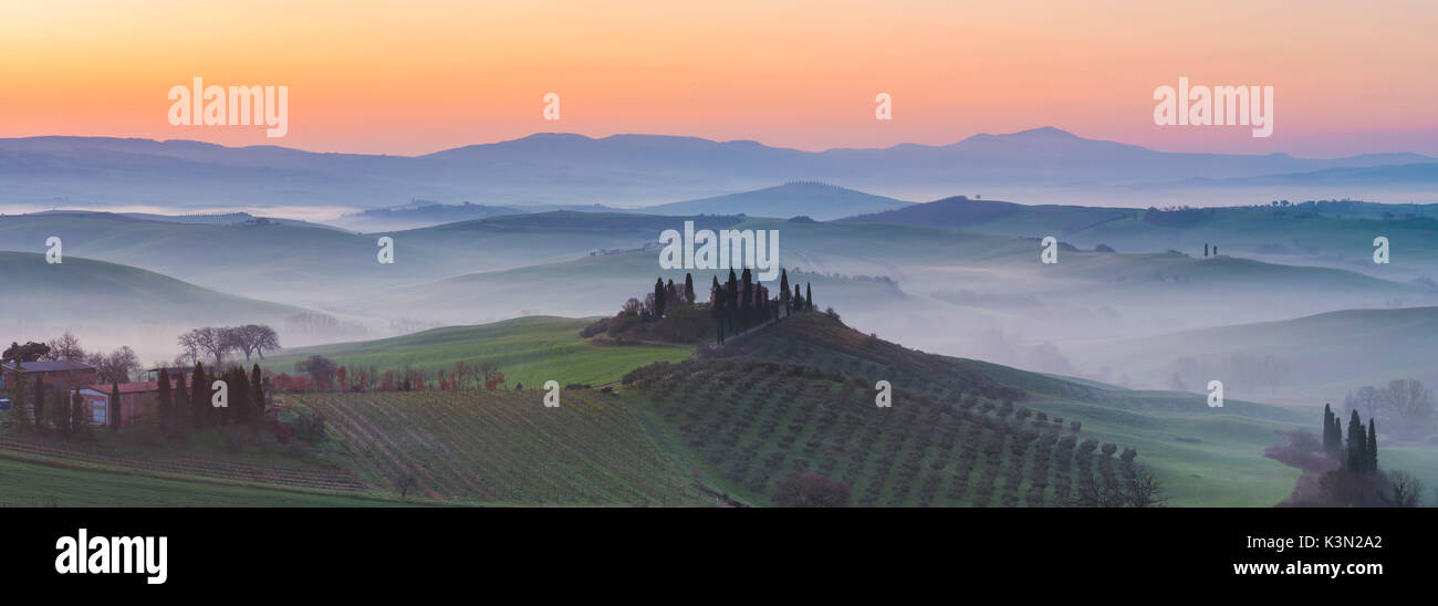 Valdorcia, Sienne, Toscane, Italie. Vue panoramique sur une ferme toscane en haut d'une colline au lever du soleil. Banque D'Images