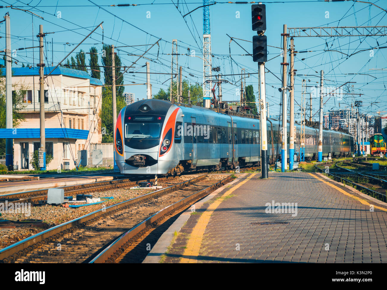 High speed train arrive sur la gare au coucher du soleil en Europe. Train intercity modernes sur le quai de la gare. Paysage industriel avec passeng Banque D'Images