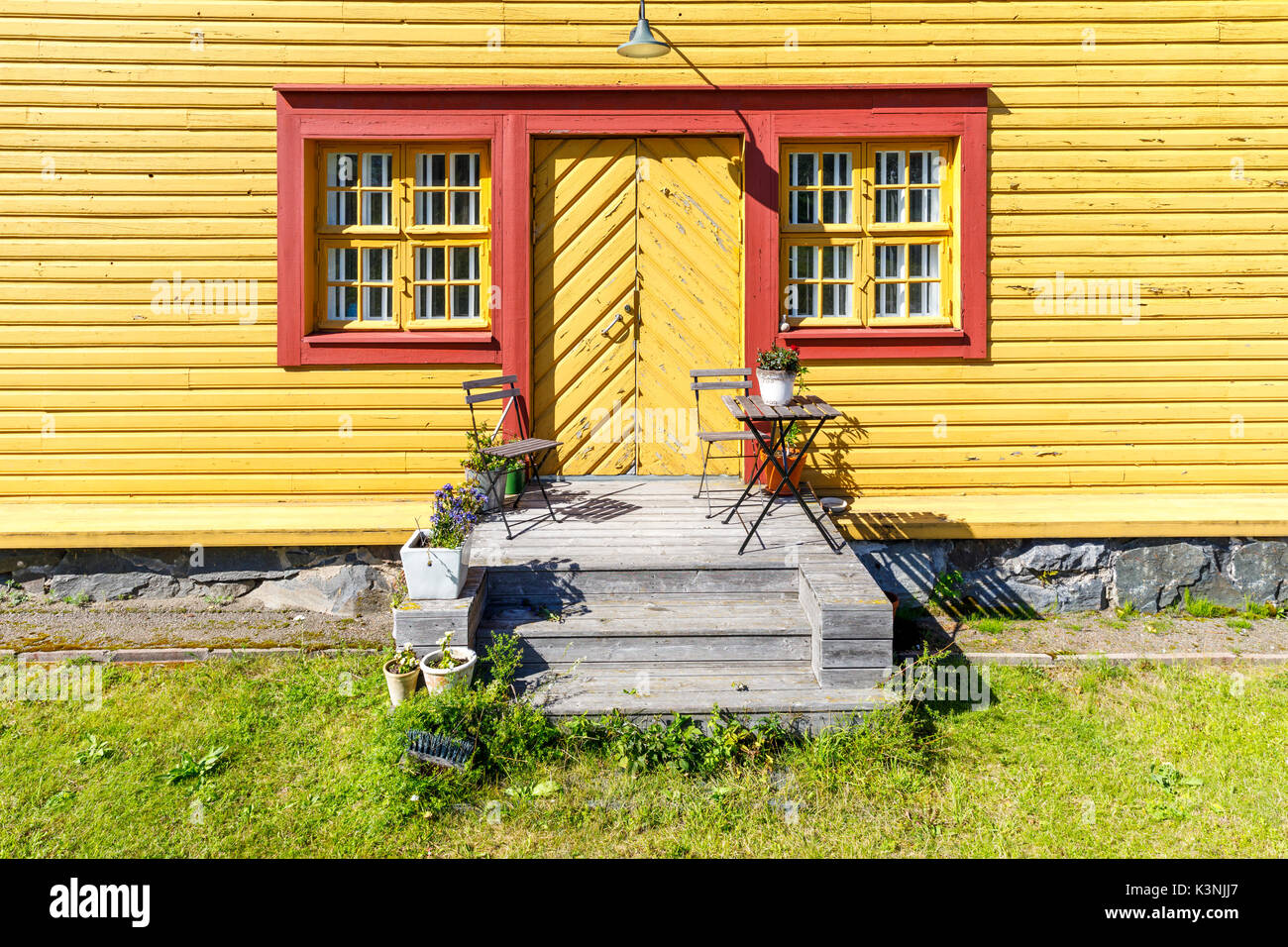 Maison en bois jaune rouge avec des châssis de fenêtre et des chaises à côté de porte Banque D'Images