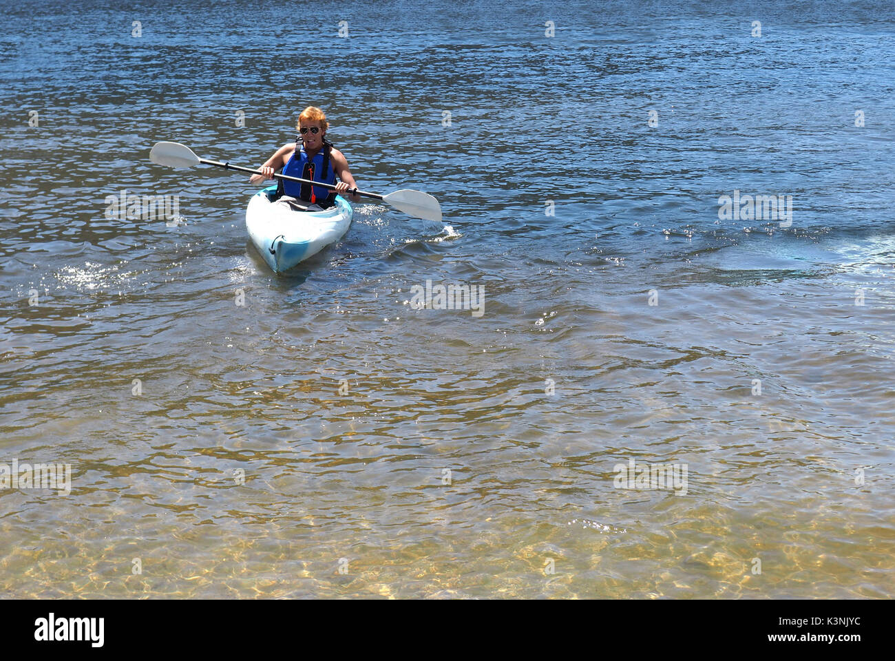 Un adolescent palettes dans un kayak sur le lac Grand dans le Colorado. Le garçon porte des lunettes de soleil et est dans un kayak simple. Banque D'Images