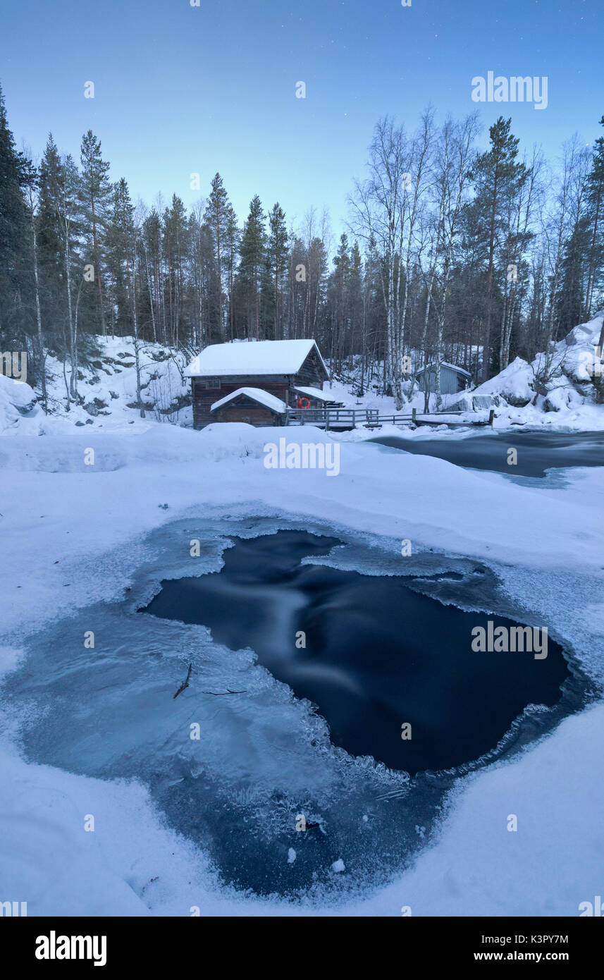 Le crépuscule frames l'eau gelée dans la Snowy Woods et la cabane en bois Juuma Myllykoski Laponie région Europe Finlande Banque D'Images